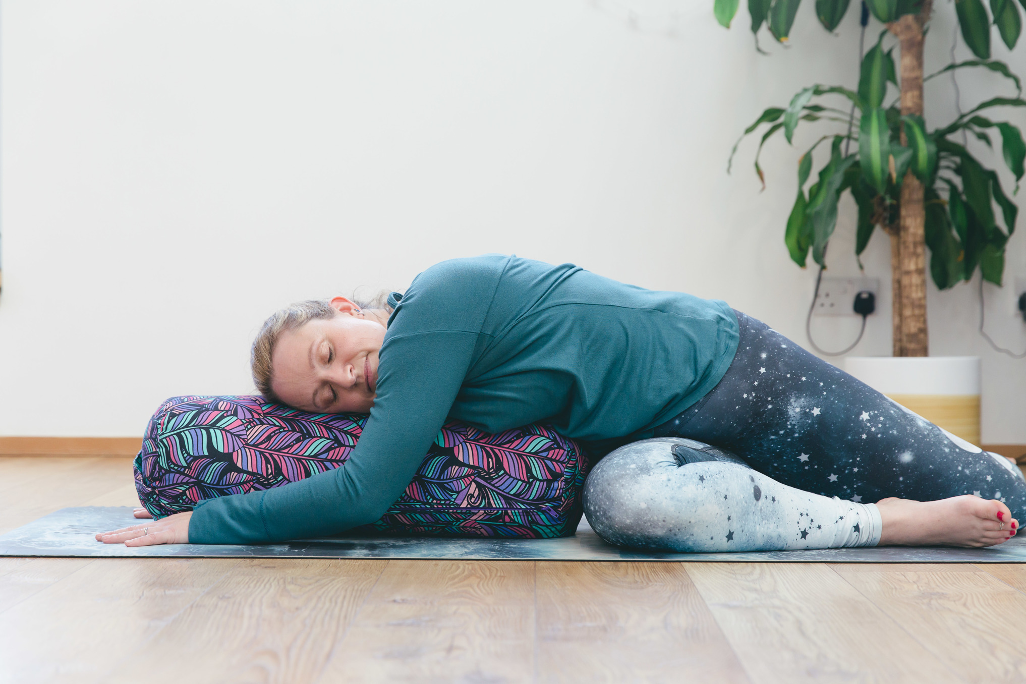 Holly, a yoga instructor, in a restorative yoga pose, bolster twist, resting on a bolster cushion.